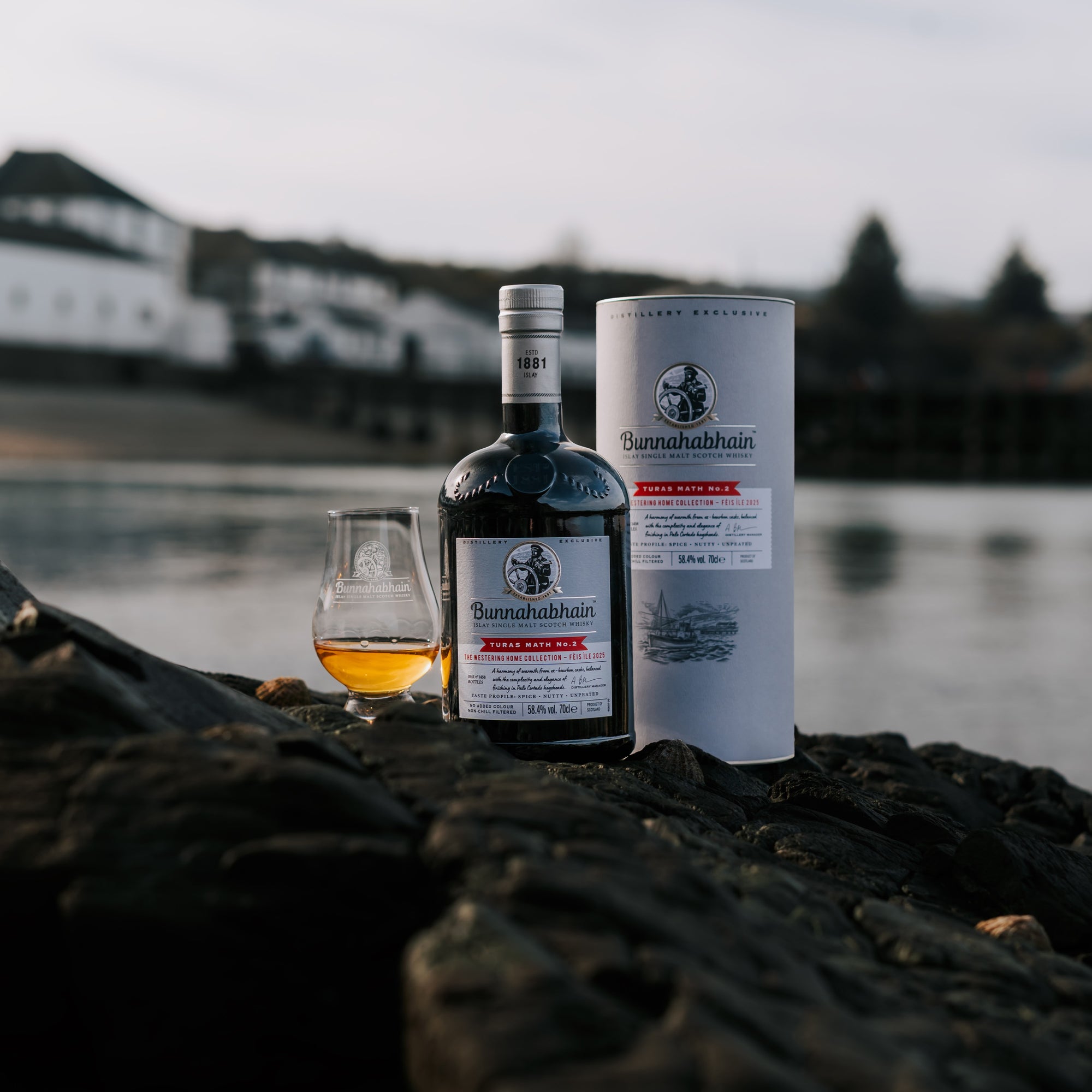 Bunnahabhain Turas Math No.2, a dram and pack sitting on rocks with Bunnahabhain Distillery backdrop