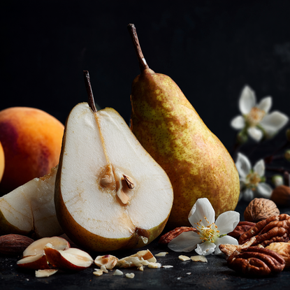 Two pears, one sliced, with flowers and nuts on a dark background
