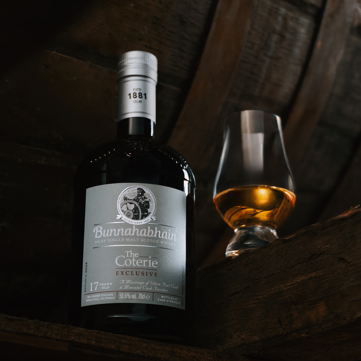Bottle of The Coterie Bunnahabhain Exclusive with a glass on a wooden surface